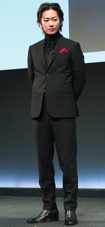 佐藤健が黒いスーツを着て立っている画像
